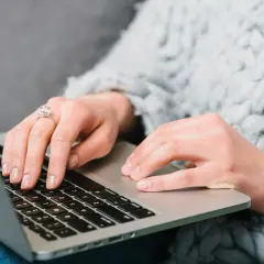 Kobieta w ciepłym swetrze uczy się, jak kupić obligacje skarbowe, wpisując dane na laptopie.
