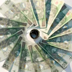 Złote banknoty o nominale 100 zł ułożone w okrąg, z pierścieniem pośrodku. Oficjalny sposób na oszczędzanie.