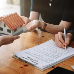 Przekazanie makiety domu podczas finalizacji cesji. Podpisanie umowy i stos banknotów na drewnianym stole.