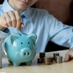 Oszczędzanie na przyszłość, może nawet na obligacje 800+. Dziecko wrzuca monetę do skarbonki w kształcie świnki.