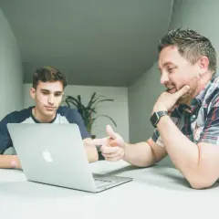 Dwóch mężczyzn przy laptopie dyskutuje o tym, ile zarabia doradca inwestycyjny.