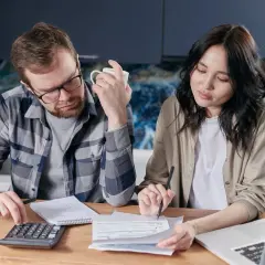 Para analizować finanse i szukać pomocy w fundusz wsparcia kredytobiorców, para siedzi przy stole z kalkulatorem i dokumentami.