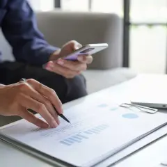 Mężczyzna analizuje dokumenty, trzymając telefon. Szuka informacji o kredyt na dowód bez umowy o pracę.