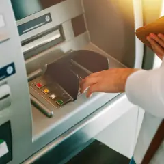 Dłoń wpisuje PIN przy bankomacie, z nadzieją, że nie zniknęły pieniądze z konta.