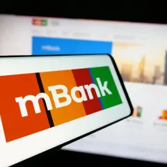 Logo mBank na ekranie smartfona, obok ekran komputera z widokiem na miasto. Szukasz informacji, jak spłacić kredyt odnawialny mBank?