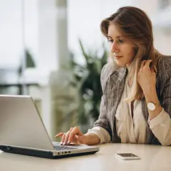 Kobieta pracuje na laptopie, planując przelew natychmiastowy. Obok leży telefon.