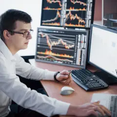 Mężczyzna w okularach analizuje wykresy na monitorach, pracując nad rejestrem krótkiej sprzedaży.