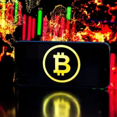 Telefon z symbolem Bitcoin na tle wykresów giełdowych. Czy warto jeszcze inwestować w bitcoin? To pytanie zadaje sobie wielu.