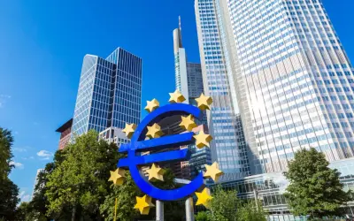 Symbol euro przed nowoczesnymi wieżowcami, siedzibą europejskiego banku centralnego.