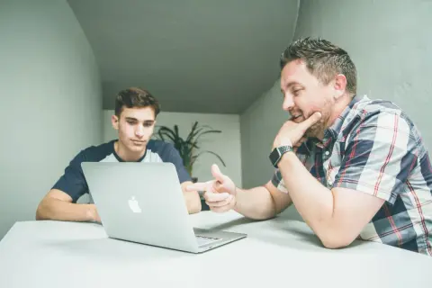 Dwóch mężczyzn przy laptopie dyskutuje o tym, ile zarabia doradca inwestycyjny.