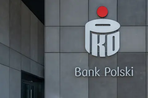 Logo PKO Banku Polskiego na szarej ścianie. Dowiedz się, jak kupić obligacje skarbowe w PKO BP.