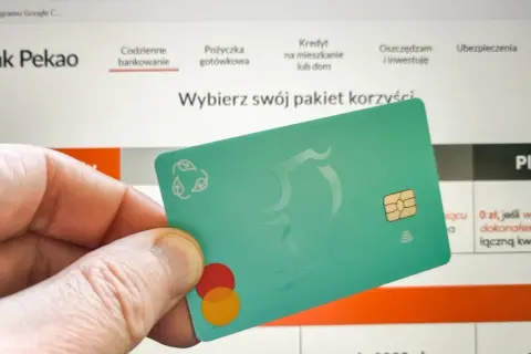 Dłoń trzyma zieloną kartę z logo Mastercard. Na ekranie komputera widać stronę banku Pekao, gdzie można dowiedzieć się, jak aktywować kartę Pekao przez internet.