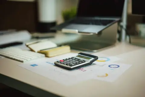 Kalkulator na biurku obok laptopa i wykresów. Czas policzyć, **brutto co to** znaczy w tym kontekście.