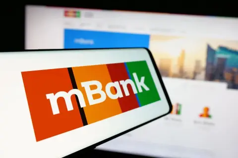 Logo mBank na ekranie smartfona, obok ekran komputera z widokiem na miasto. Szukasz informacji, jak spłacić kredyt odnawialny mBank?