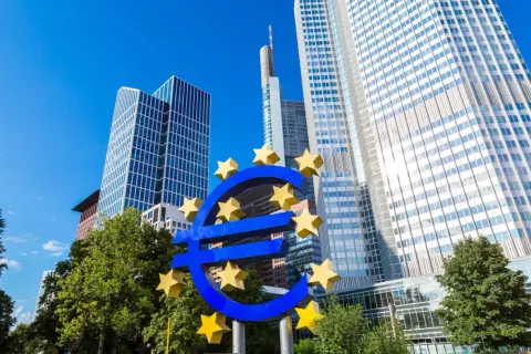 Symbol euro przed nowoczesnymi wieżowcami, siedzibą europejskiego banku centralnego.