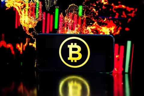 Telefon z symbolem Bitcoin na tle wykresów giełdowych. Czy warto jeszcze inwestować w bitcoin? To pytanie zadaje sobie wielu.