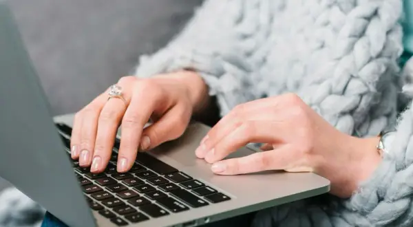 Kobieta w ciepłym swetrze uczy się, jak kupić obligacje skarbowe, wpisując dane na laptopie.