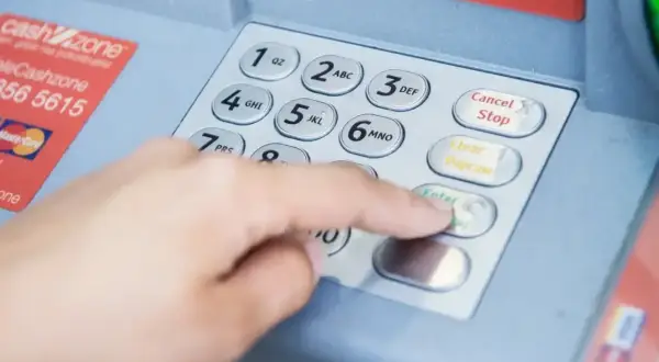 Dłoń wpisuje PIN na bankomacie, obok karta płatnicza. Może to oznaczać próbę sprawdzenia salda lub wypłaty, która doprowadzi do debetu na koncie.