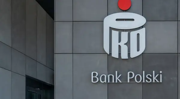 Logo PKO Banku Polskiego na szarej ścianie. Dowiedz się, jak kupić obligacje skarbowe w PKO BP.