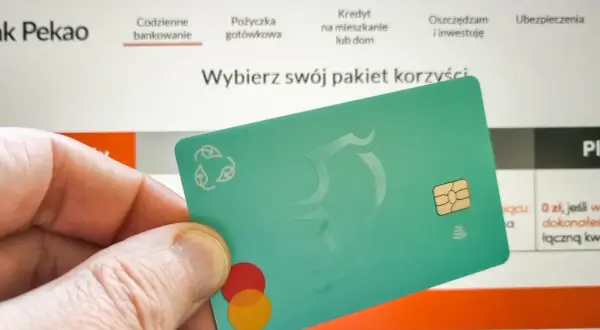 Dłoń trzyma zieloną kartę z logo Mastercard. Na ekranie komputera widać stronę banku Pekao, gdzie można dowiedzieć się, jak aktywować kartę Pekao przez internet.