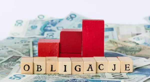 Drewniane klocki z napisem "OBLIGACJE" na tle polskich banknotów. Symbolizują one, kto emituje obligacje skarbowe.