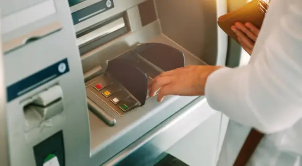 Dłoń wpisuje PIN przy bankomacie, z nadzieją, że nie zniknęły pieniądze z konta.