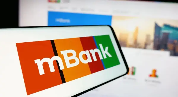 Logo mBank na ekranie smartfona, obok ekran komputera z widokiem na miasto. Szukasz informacji, jak spłacić kredyt odnawialny mBank?