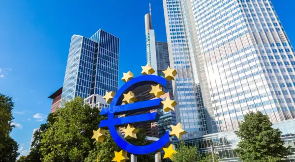 Symbol euro przed nowoczesnymi wieżowcami, siedzibą europejskiego banku centralnego.