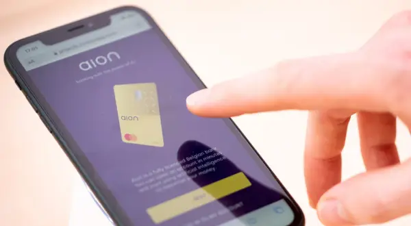 Palec dotyka ekranu telefonu z aplikacją Aion bank, prezentującą złoty debetowy Aion.