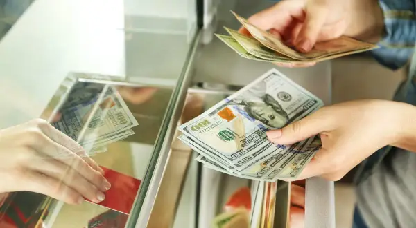 Ręce przekazują sobie banknoty dolarowe. Czy można kupić walutę w NBP? Tutaj widzimy wymianę pieniędzy.