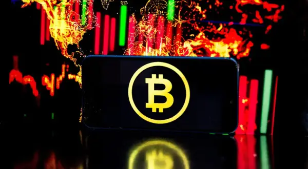 Telefon z symbolem Bitcoin na tle wykresów giełdowych. Czy warto jeszcze inwestować w bitcoin? To pytanie zadaje sobie wielu.