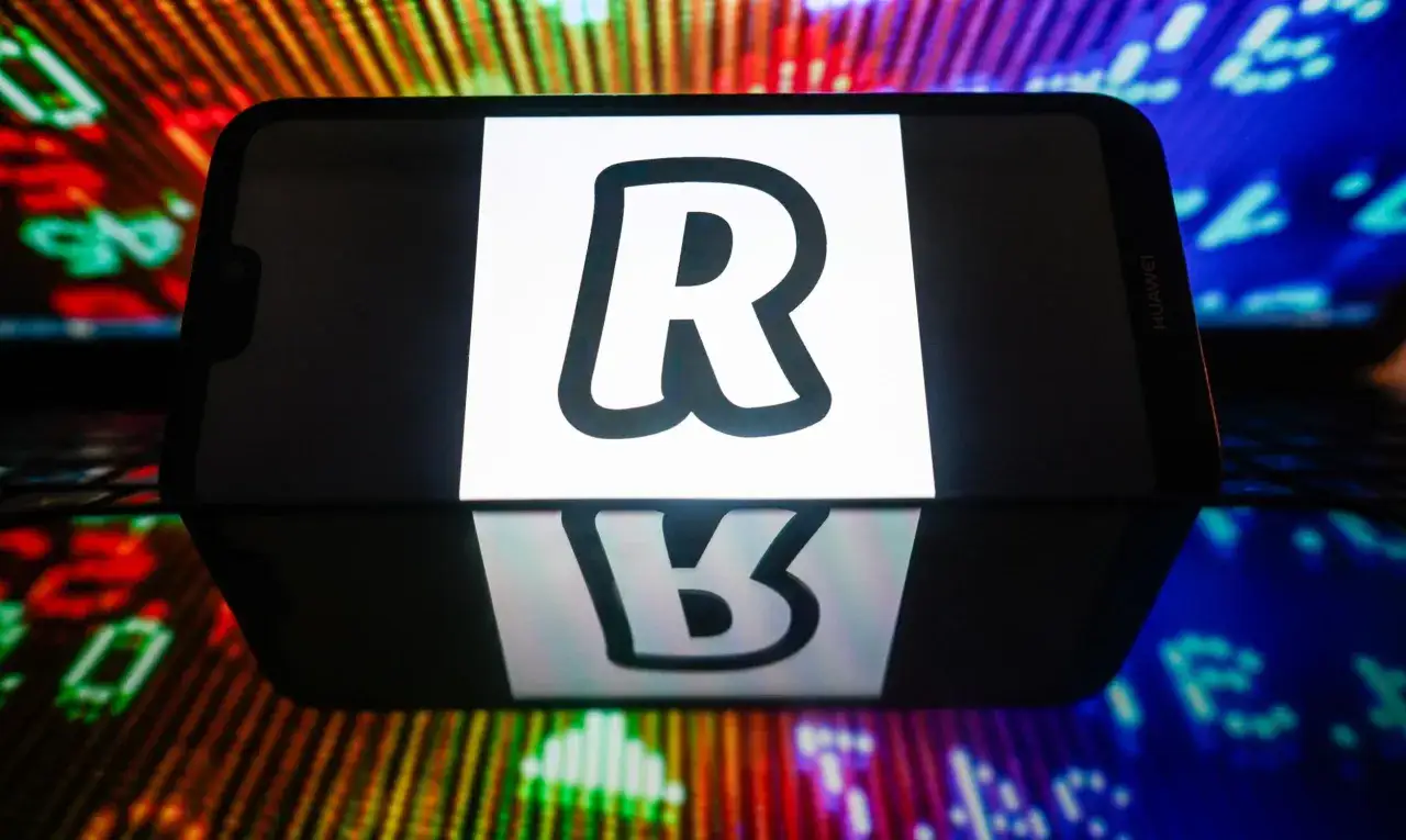 Telefon z logo Revolut. Jak wypłacić kryptowaluty z Revolut? Wyświetlają się wykresy giełdowe.