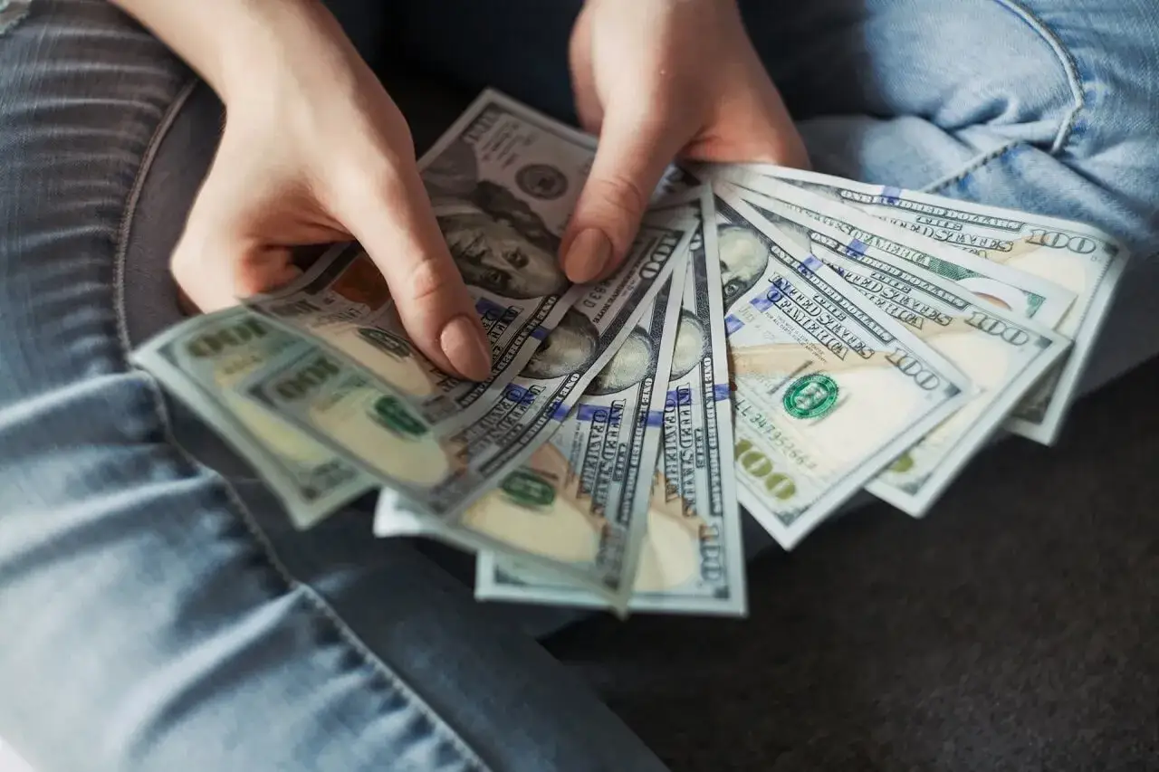 Dłonie trzymające banknoty 100 dolarowe. Zastanawiasz się, ile trwa likwidacja lokaty?