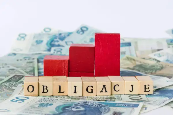 Drewniane klocki z napisem "OBLIGACJE" na tle polskich banknotów. Symbolizują one, kto emituje obligacje skarbowe.