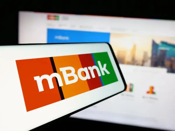 Logo mBank na ekranie smartfona, obok ekran komputera z widokiem na miasto. Szukasz informacji, jak spłacić kredyt odnawialny mBank?