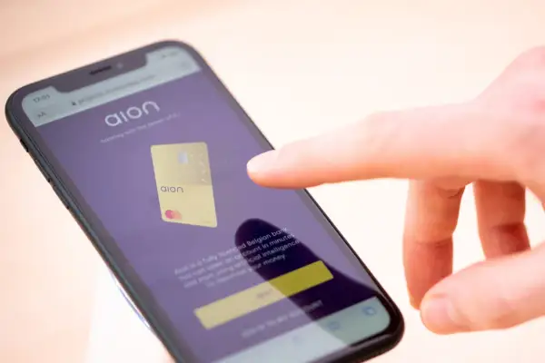 Palec dotyka ekranu telefonu z aplikacją Aion bank, prezentującą złoty debetowy Aion.