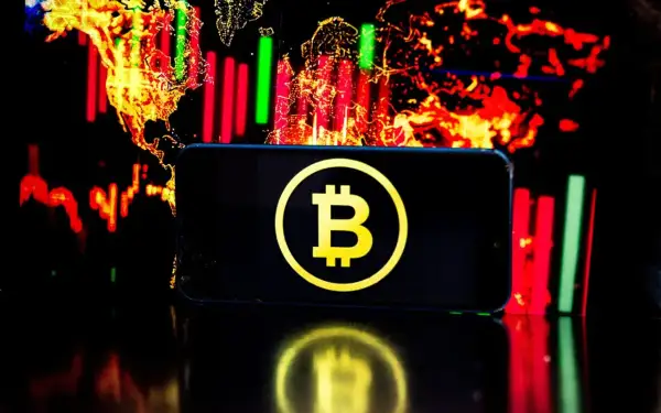Telefon z symbolem Bitcoin na tle wykresów giełdowych. Czy warto jeszcze inwestować w bitcoin? To pytanie zadaje sobie wielu.